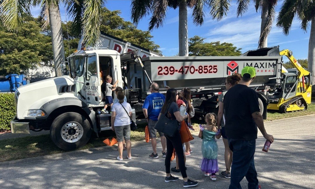 Families looking at a Maxim Disposal roll-off truck and container at a community event, with a child sitting in the cab