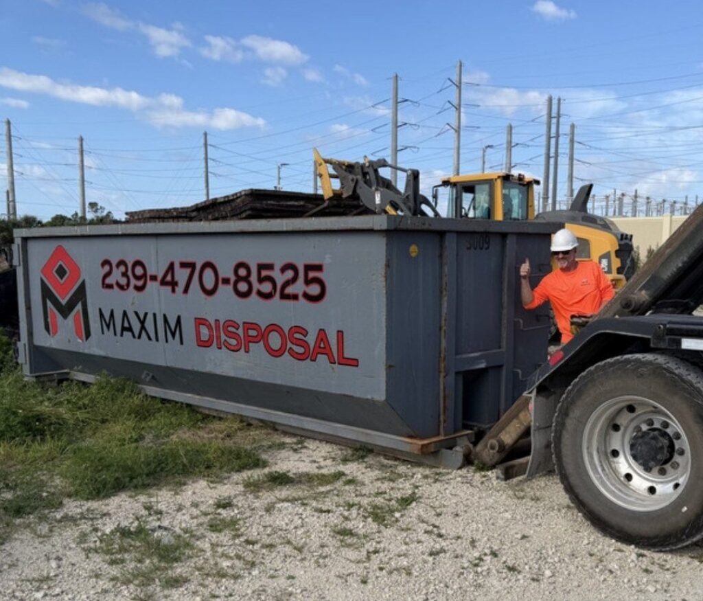 Maxim Disposal driver in a hard hat giving a thumbs up beside a loaded 30 yard roll-off container