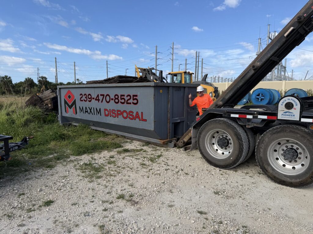 Maxim Disposal crew member in high-visibility gear setting a roll-off container on site