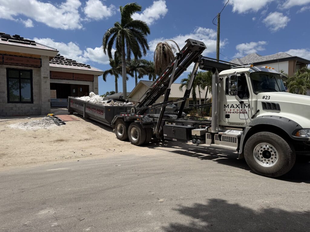 Maxim Disposal roll-off truck delivering a container to a block-shell house under construction in Southwest Florida