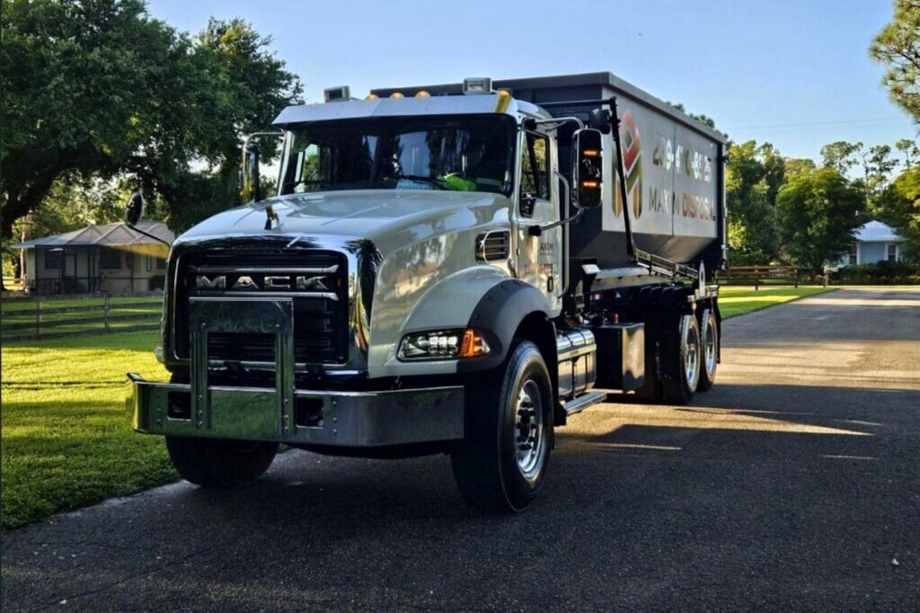 Maxim Disposal Mack roll-off truck with a container loaded, parked in a residential driveway in Southwest Florida
