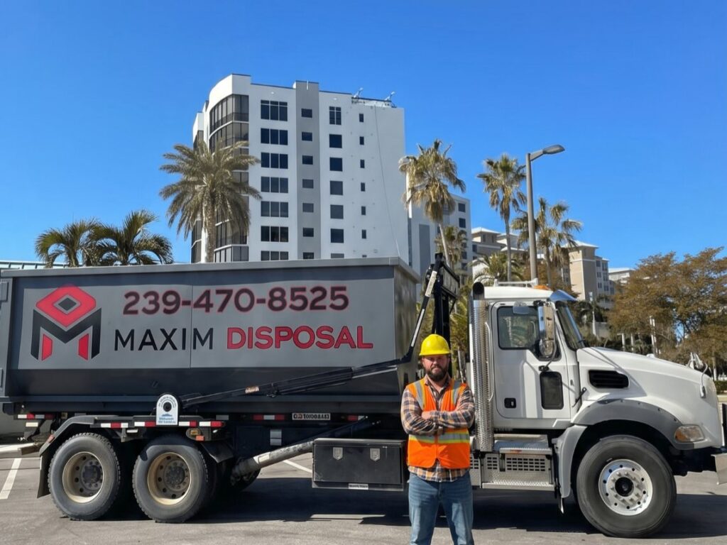 Maxim Disposal driver in hard hat and high-visibility vest beside a roll-off truck in Fort Myers