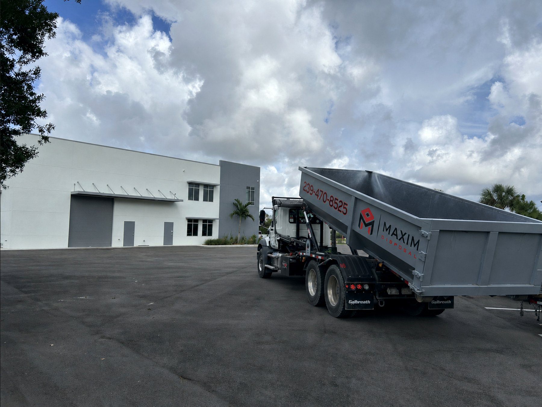 Maxim Disposal roll-off truck setting a 30 yard container at a commercial building in Fort Myers, Florida
